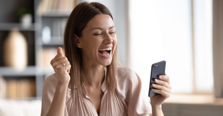 Excited happy woman looking at phone screen, celebrating online win, overjoyed young female screaming with joy, holding smartphone, reading good news in unexpected message or email